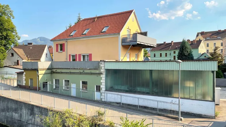 Mehrere Gebäude mit unterschiedlichen Fassadenfarben und einem Balkon, umgeben von Grün.