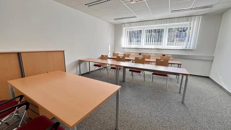 Heller Konferenzraum mit mehreren Tischen und Stühlen, ausgestattet mit Klimaanlage und Teppichboden.