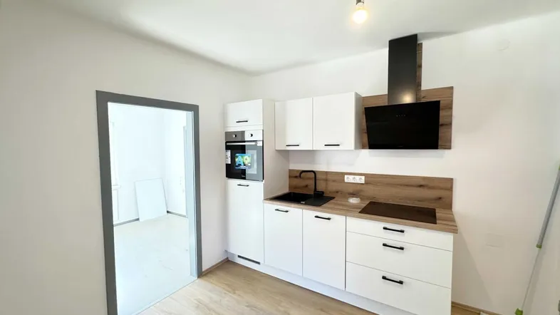 Moderne Einbauküche mit weißen Schränken, Holz-Arbeitsplatte und integrierten Geräten in einem hellen Raum.