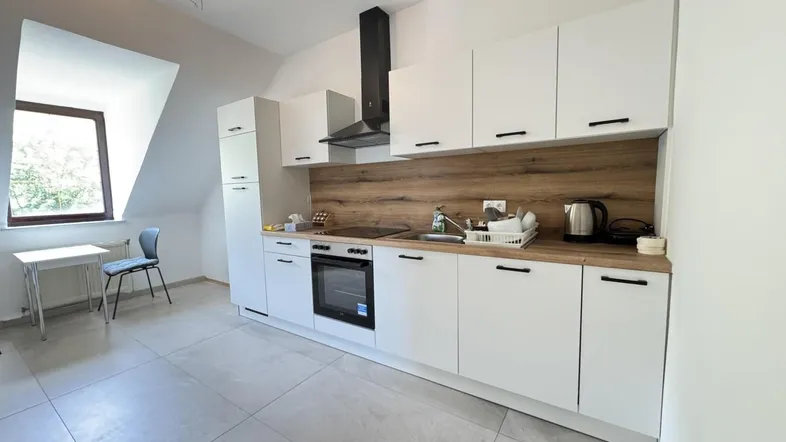 Moderne Küche mit weißen Schränken, Holzakzenten und einem kleinen Essbereich am Fenster.