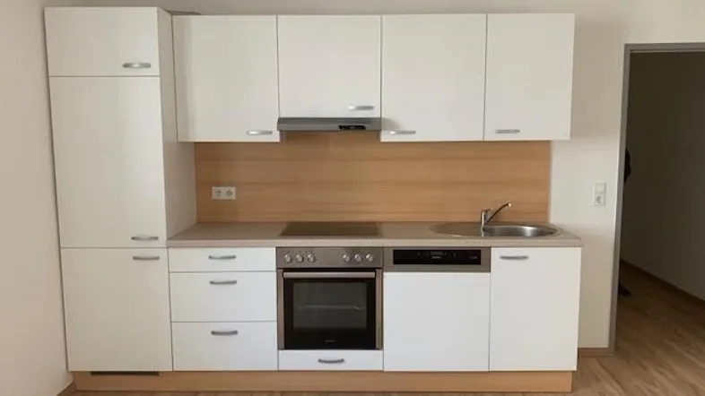 Moderne Einbauküche mit weißen Schränken, Holzrückwand und integrierten Geräten in neuwertigem Zustand.