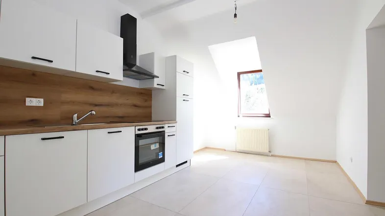 Moderne Einbauküche mit weißen Fronten, Holzdetails und Dachschräge in einem hellen Raum.
