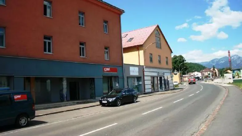 Blick auf eine Straße mit Gebäuden, Geschäften und Bergen im Hintergrund unter einem klaren blauen Himmel.