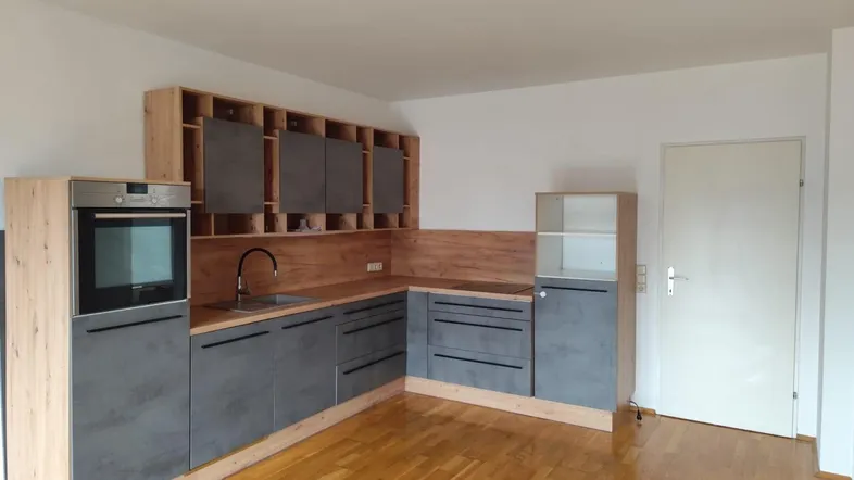 Moderne Küche mit Holzparkettboden, grauen und holzfarbenen Schränken sowie einem Einbauofen.