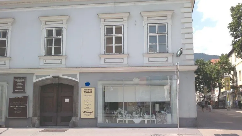 Historisches Gebäude mit hellblauer Fassade, traditionellen Fenstern und einem Ladenlokal im Erdgeschoss.