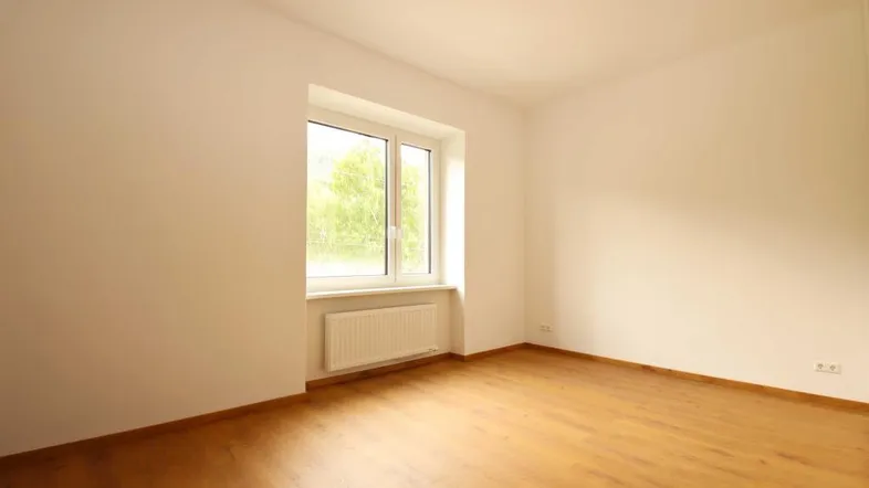 Heller, leerer Raum mit großem Fenster und Heizkörper, bereit zur individuellen Gestaltung.