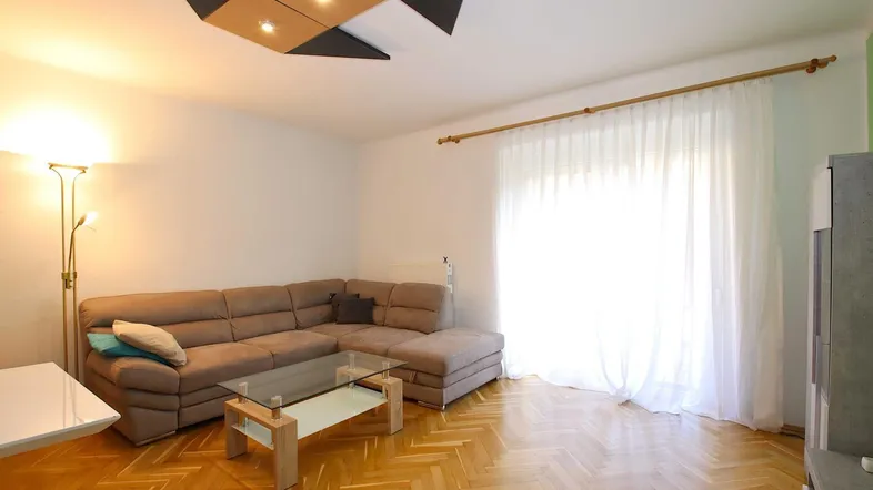 Helles Wohnzimmer mit modernem Deckenlicht, beigem Ecksofa und Parkettboden.