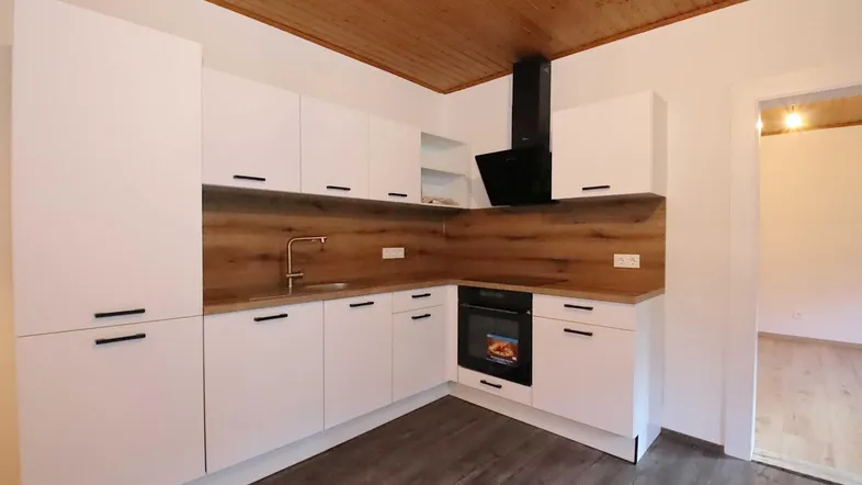 Moderne Küche mit weißen Schränken, Holzoptik-Arbeitsplatte und Holzdeckenverkleidung.