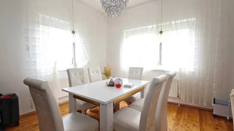 Helles Esszimmer mit weißem Esstisch, passenden Stühlen und einem eleganten Kronleuchter.