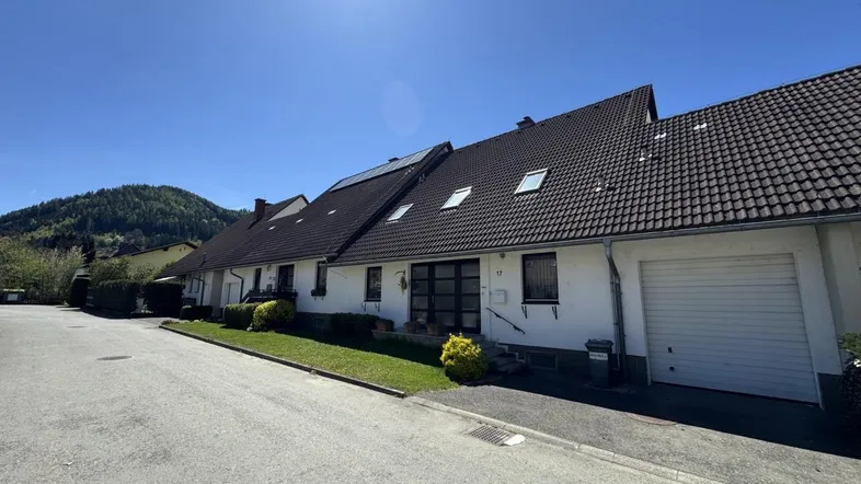 Reihenhausfassade mit Satteldach, Dachfenstern und integrierter Garage unter blauem Himmel.