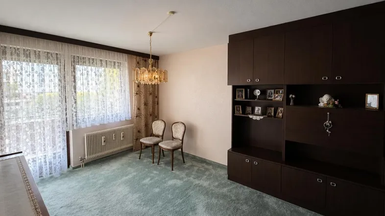 Helles Wohnzimmer mit Teppichboden, dunklen Schränken und Zugang zum Balkon.