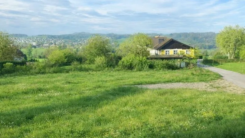 Weitläufige Grünfläche mit Blick auf ein charmantes gelbes Haus und die umliegende Landschaft.