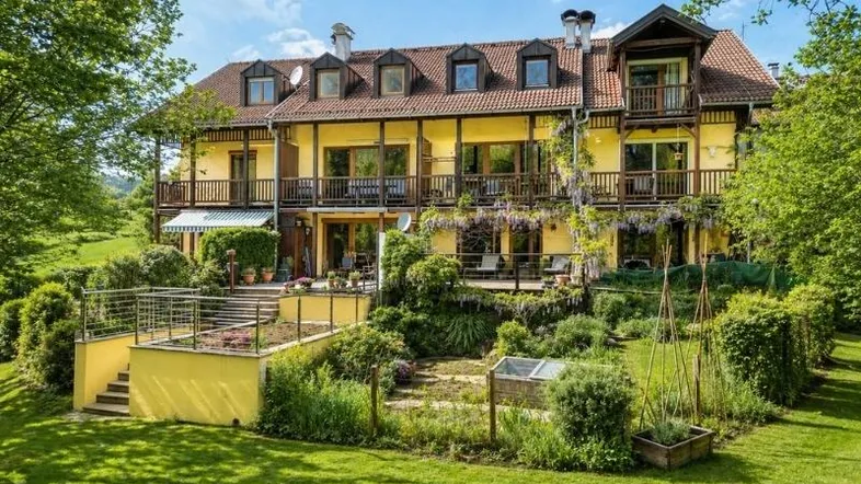 Großzügiges Anwesen mit gelber Fassade, mehreren Balkonen und einem gepflegten Gartenbereich mit Hochbeeten.