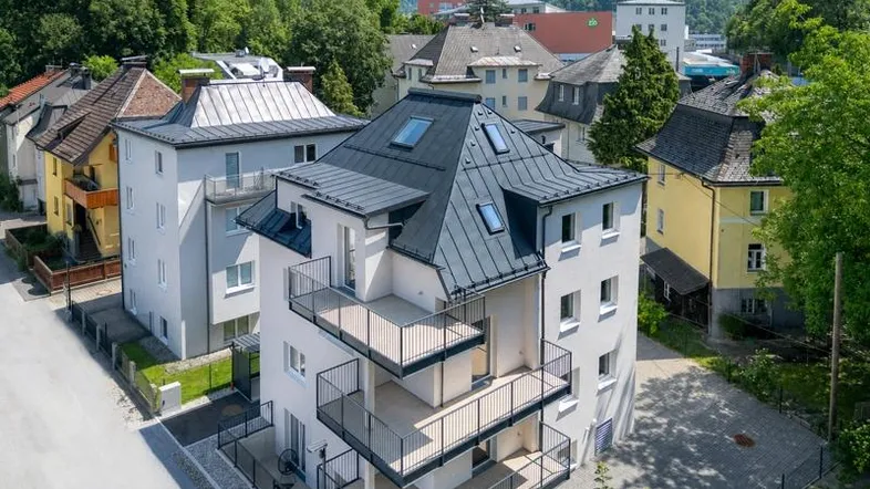 Modernes Mehrfamilienhaus mit mehreren Balkonen und Blick auf die umliegende Berglandschaft.