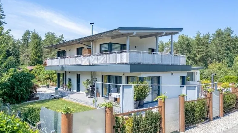 Modernes Einfamilienhaus mit mehreren Balkonen, Garten und umzäuntem Grundstück.