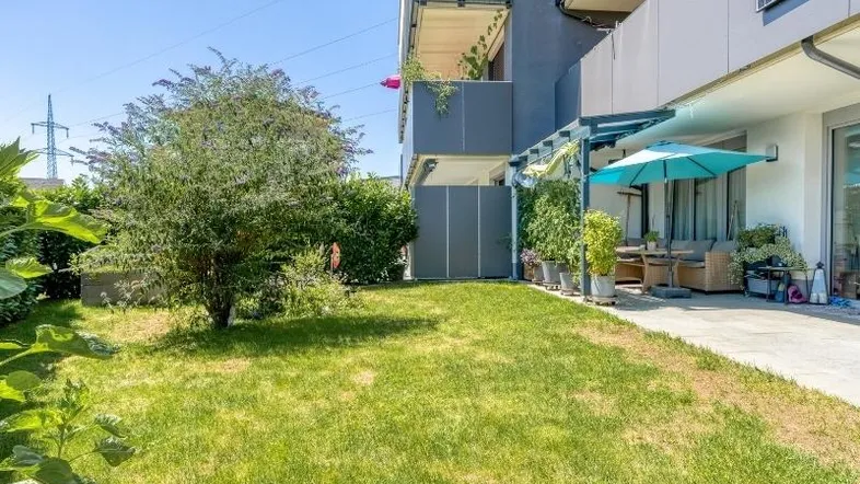 Gepflegter Gartenbereich mit Rasenfläche und angrenzender Terrasse eines modernen Wohngebäudes.