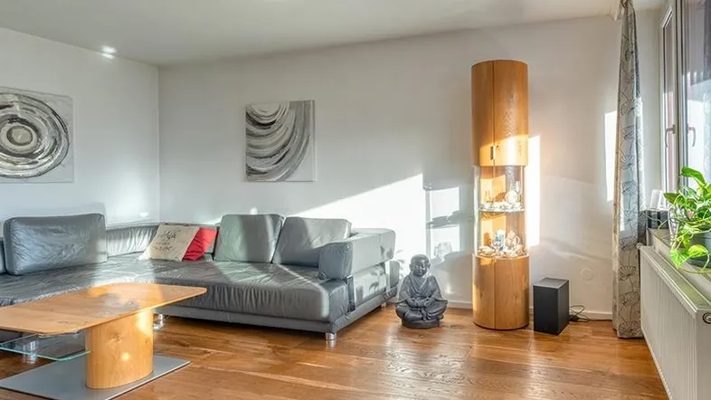 Helles Wohnzimmer mit Holzboden, bequemer Couch und dekorativen Elementen, durchflutet von natürlichem Licht.
