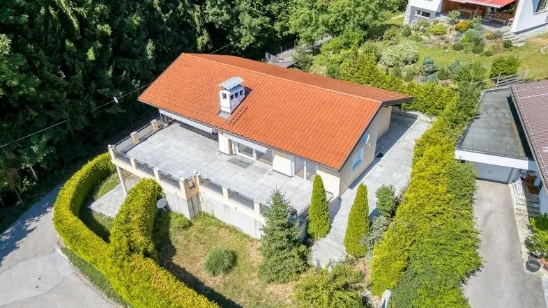 Luftaufnahme des Hauses mit rotem Ziegeldach, großer Terrasse und umgebender grüner Landschaft.