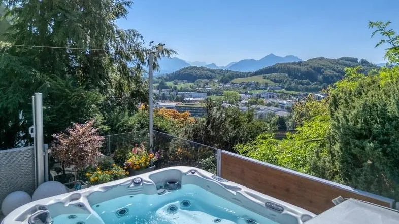 Whirlpool im Freien mit atemberaubendem Blick auf die Berge und das Tal, umgeben von üppigem Grün.