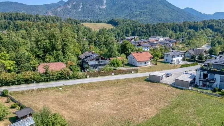 Luftaufnahme eines Grundstücks mit umliegenden Häusern, viel Grün und beeindruckender Bergkulisse.