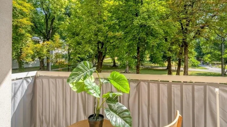 Gemütlicher Balkon mit Tisch und Stuhl, umgeben von üppigem Grün und Bäumen.