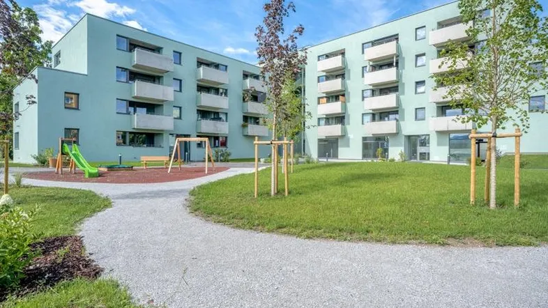 Moderne Wohngebäude mit Balkonen, umgeben von Grünflächen und einem Kinderspielplatz.