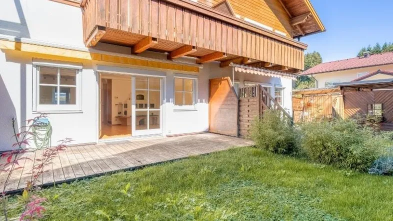 Holzterrasse mit Rasenfläche und Zugang zum Garten, unter einem Holzbalkon gelegen.