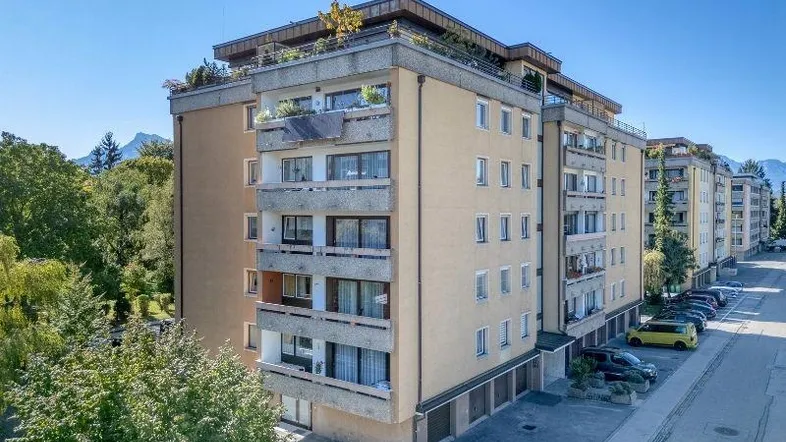 Mehrfamilienhaus mit Balkonen, Garagen und Blick auf die umliegende Berglandschaft.