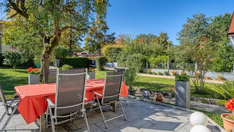Geräumige Terrasse mit Esstisch und Stühlen, umgeben von einem gepflegten Garten unter blauem Himmel.