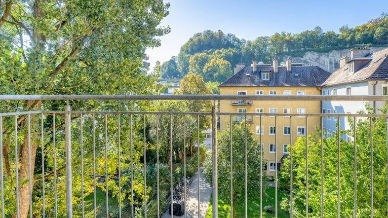 Blick vom Balkon auf einen grünen Innenhof mit Bäumen und umliegenden Gebäuden.