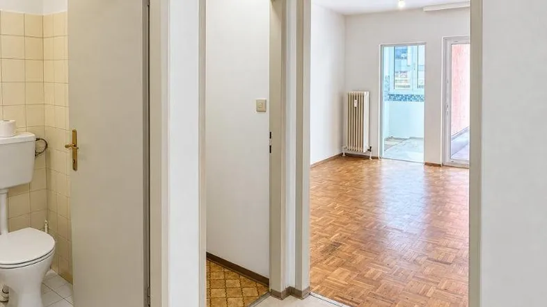 Blick vom Flur in ein helles Wohnzimmer mit Parkettboden und Zugang zu einem WC.