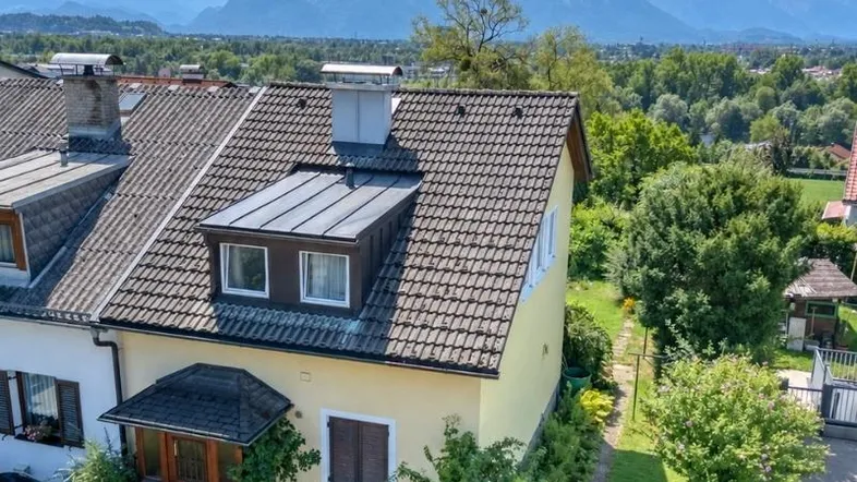 Luftaufnahme eines Hauses mit Ziegeldach, Gauben und Bergblick im Hintergrund.