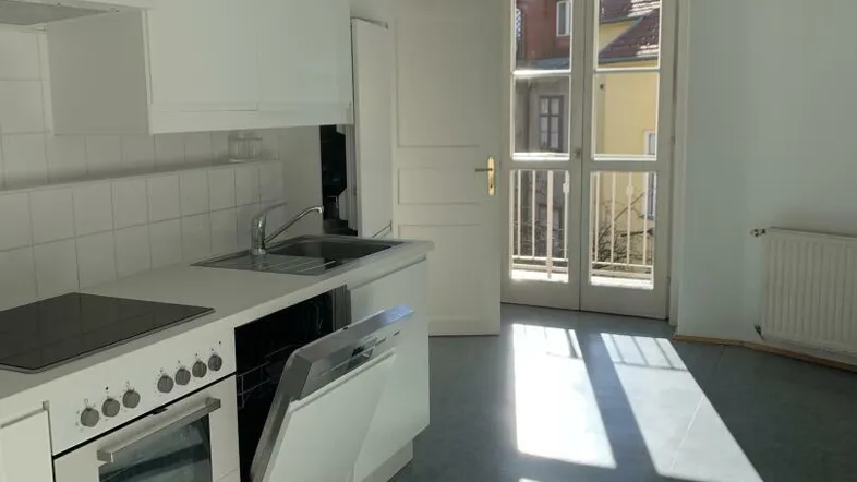 Helle Küche mit weißen Einbauschränken und Geräten, inklusive Geschirrspüler und Zugang zum Balkon.
