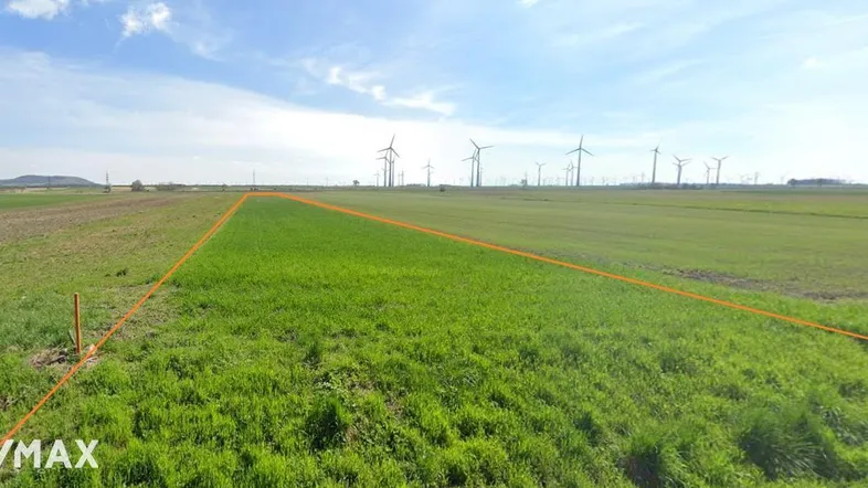 Weitläufiges grünes Feld mit markierter Grundstücksgrenze und Windrädern am Horizont unter blauem Himmel.