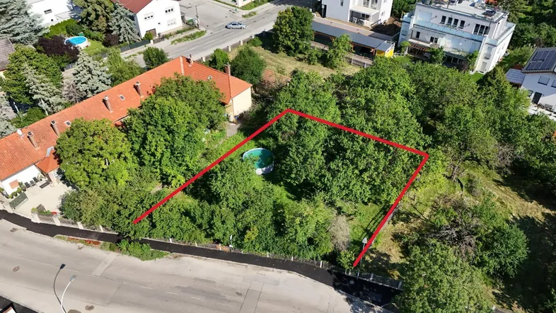 Luftaufnahme eines Grundstücks mit roter Markierung, umgeben von Wohngebäuden und viel Grün.