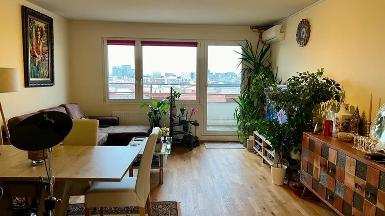 Geräumiger Wohn-Essbereich mit Holzboden, bequemer Couch und Zugang zu einem Balkon mit Stadtblick.