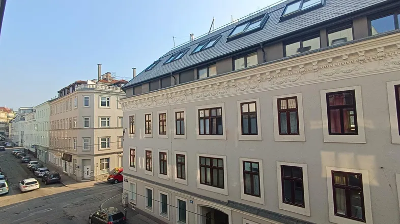 Blick auf die Fassade eines Mehrfamilienhauses mit Dachgauben und der umliegenden Straße.
