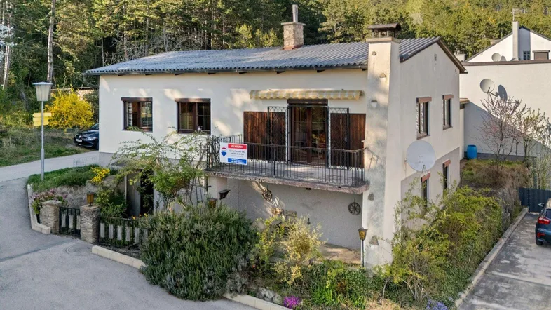 Traditionelles Einfamilienhaus mit Balkon und Gartenbereich, umgeben von viel Grün und Bäumen.