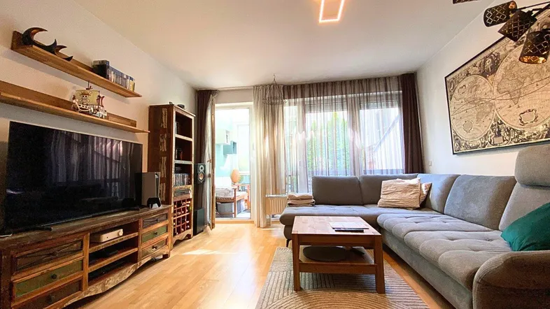 Helles Wohnzimmer mit großem Ecksofa, Holzboden und direktem Zugang zum Balkon.