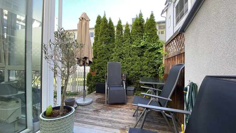 Gemütliche Terrasse mit Holzdeck, Gartenmöbeln und hohen Hecken für erhöhte Privatsphäre.