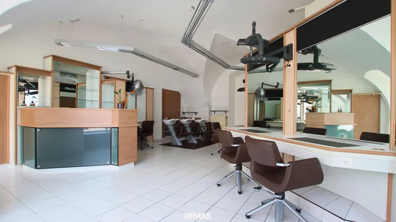 Geräumiger Friseursalon mit mehreren Styling-Stationen, Waschbecken und Empfangsbereich, ausgestattet mit Fliesenboden und gewölbten Decken.