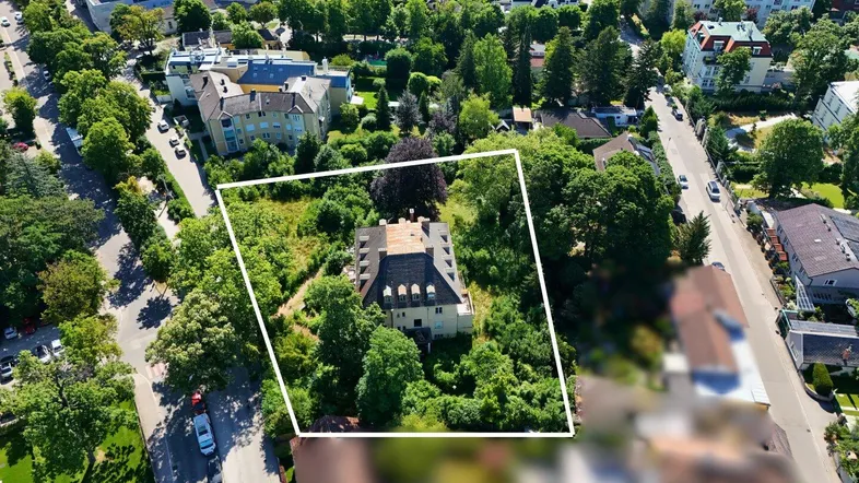 Luftaufnahme eines Anwesens mit markierten Grundstücksgrenzen, umgeben von viel Grün und weiteren Gebäuden.