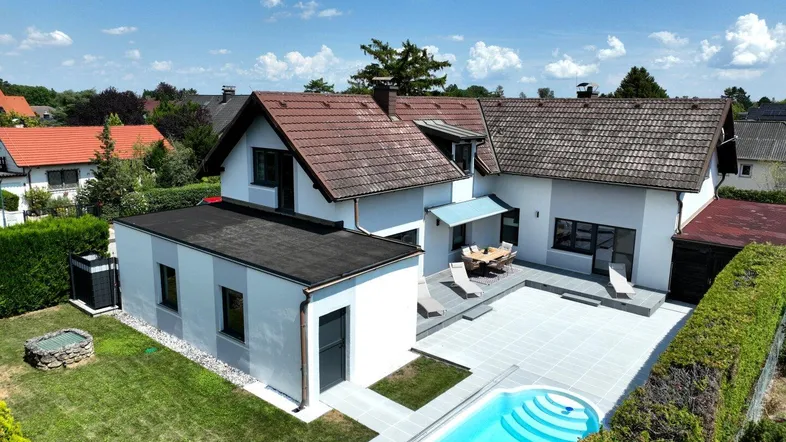 Luftaufnahme eines Hauses mit großem Garten, Pool und weitläufiger Terrasse unter blauem Himmel.