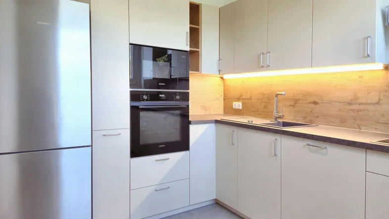 Moderne Einbauküche mit hellen Schränken, integrierten Geräten und dunkler Arbeitsplatte.