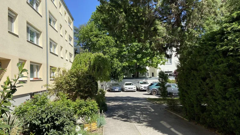 Mehrfamilienhaus mit Parkplätzen und grüner Umgebung an einem sonnigen Tag.