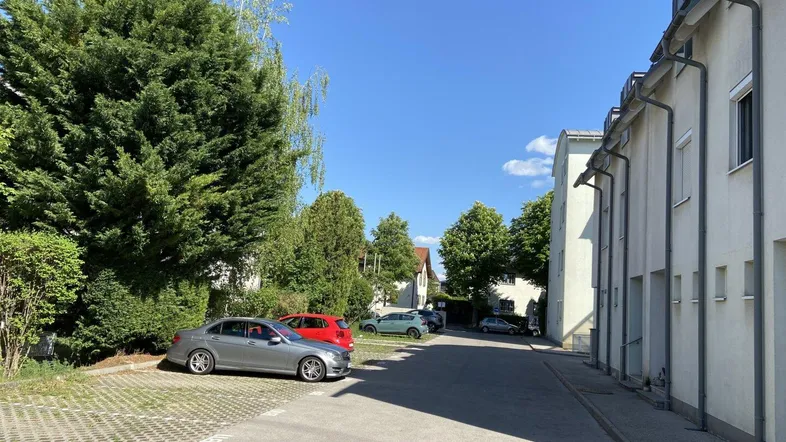 Außenansicht eines Wohngebäudes mit Parkplätzen und viel Grün unter blauem Himmel.