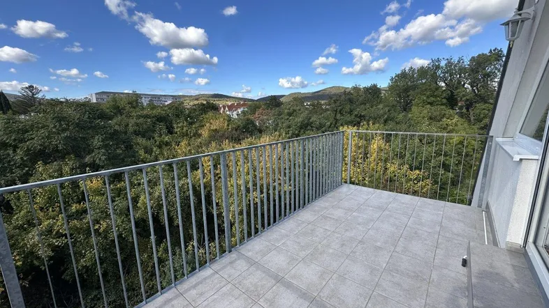 Geräumiger Balkon mit Fliesenboden und weitem Blick ins Grüne unter blauem Himmel.
