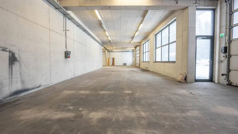 Großer, leerer Gewerberaum mit Betonboden, hohen Decken und großen Fenstern, ideal für Lager oder Produktion.