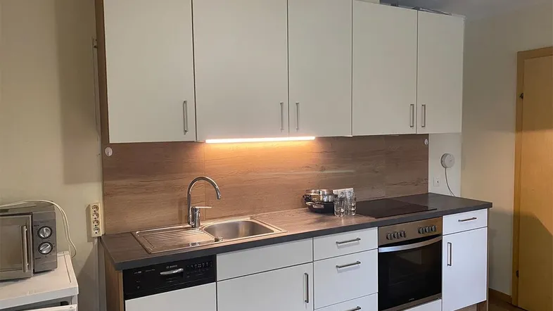 Moderne Einbauküche mit weißen Schränken, dunkler Arbeitsplatte und integrierten Geräten für effizientes Kochen.
