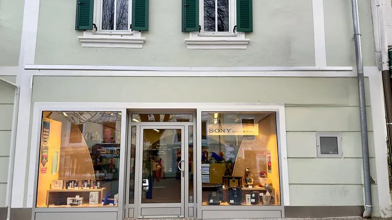 Fassade eines Geschäftsgebäudes mit großen Schaufenstern im Erdgeschoss und traditionellen grünen Fensterläden im Obergeschoss.